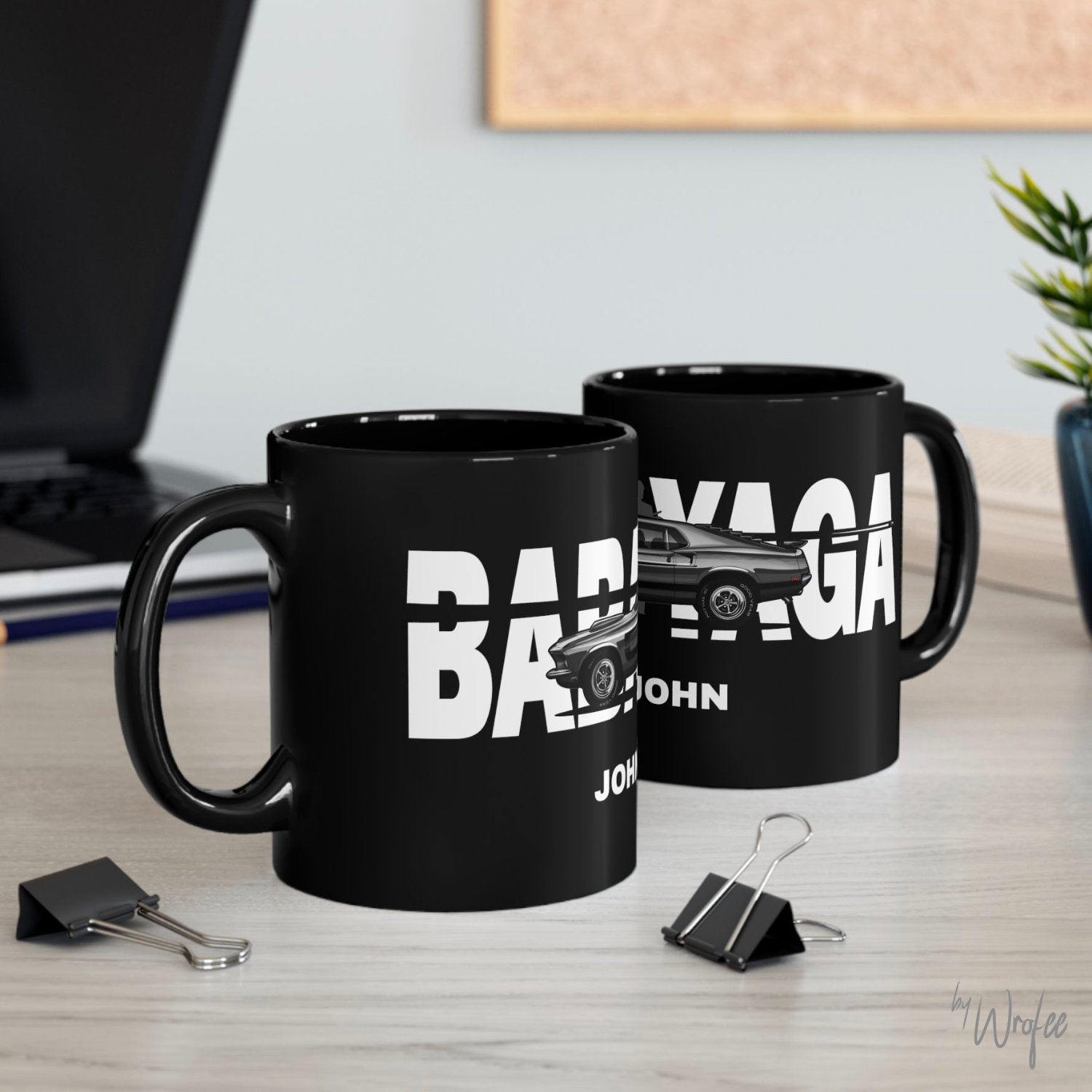Two black mugs with 'Babe' and 'John' printed on them, placed on a desk.