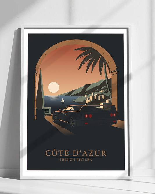A Ferrari F40 framed travel poster print leaning against a white wall, showing a stylized coastal scene with an archway, palm tree, mountains, and a black car. The text at the bottom reads “CÔTE D'AZUR” and “FRENCH RIVIERA.