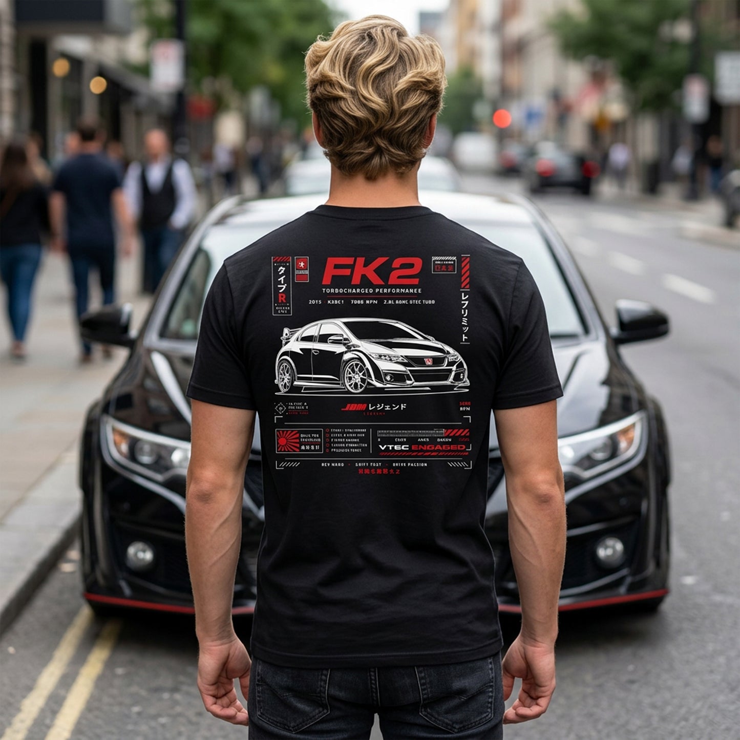 A man viewed from behind wearing a black t-shirt with a large red and white graphic print on the back, standing in front of a black car on a city street.