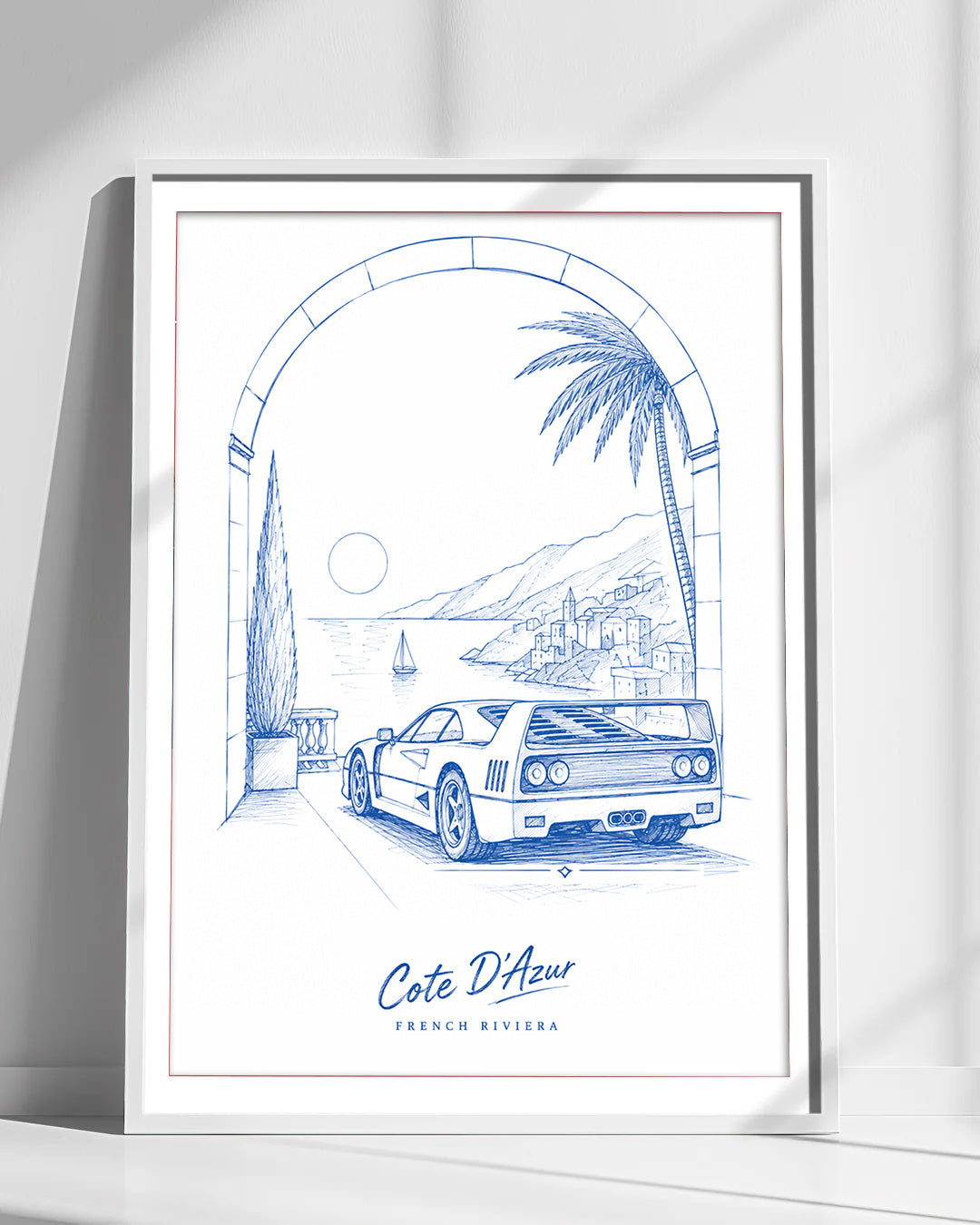 A framed art print featuring a blue line drawing of a Ferrari F40 on a coastal road under an archway, with the text 'Cote D'Azur' and 'FRENCH RIVIERA' at the bottom. The print is displayed in a white frame against a white wall with soft diagonal shadows.