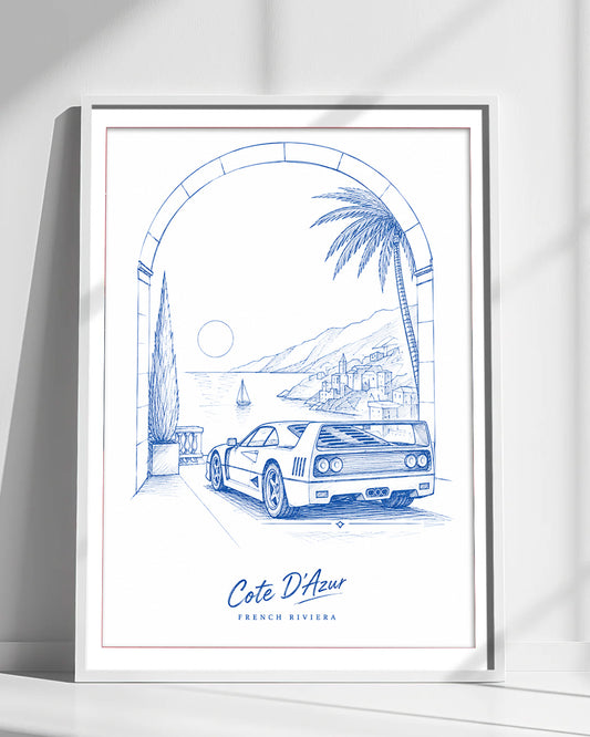 A framed art print featuring a blue line drawing of a Ferrari F40 on a coastal road under an archway, with the text 'Cote D'Azur' and 'FRENCH RIVIERA' at the bottom. The print is displayed in a white frame against a white wall with soft diagonal shadows.