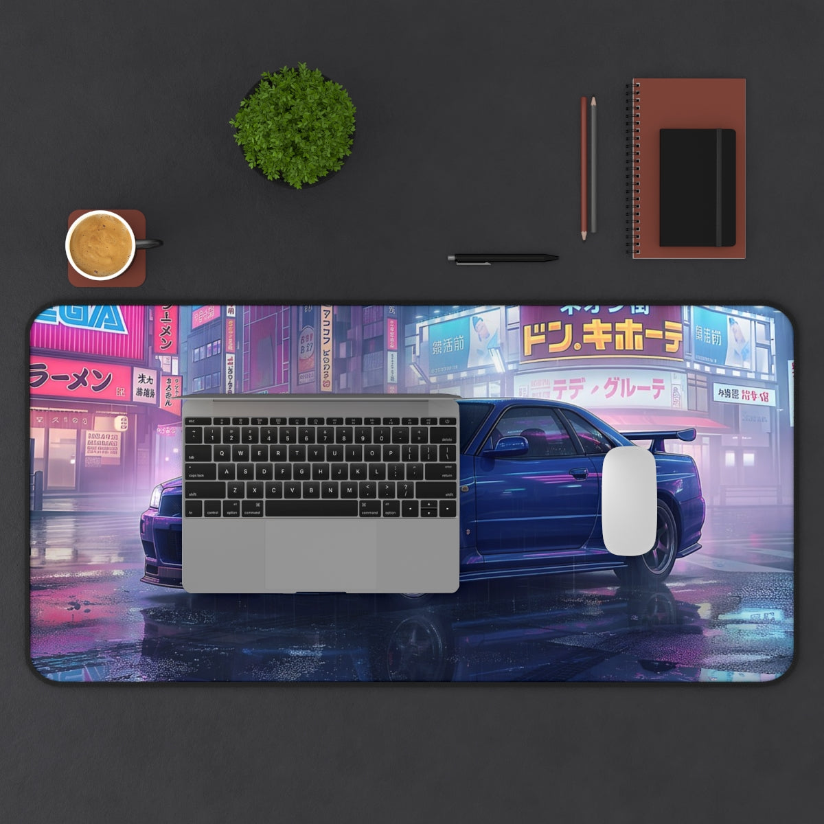 Desk setup with a large mouse pad featuring a car and cityscape design, laptop, keyboard, mouse, and office supplies.
