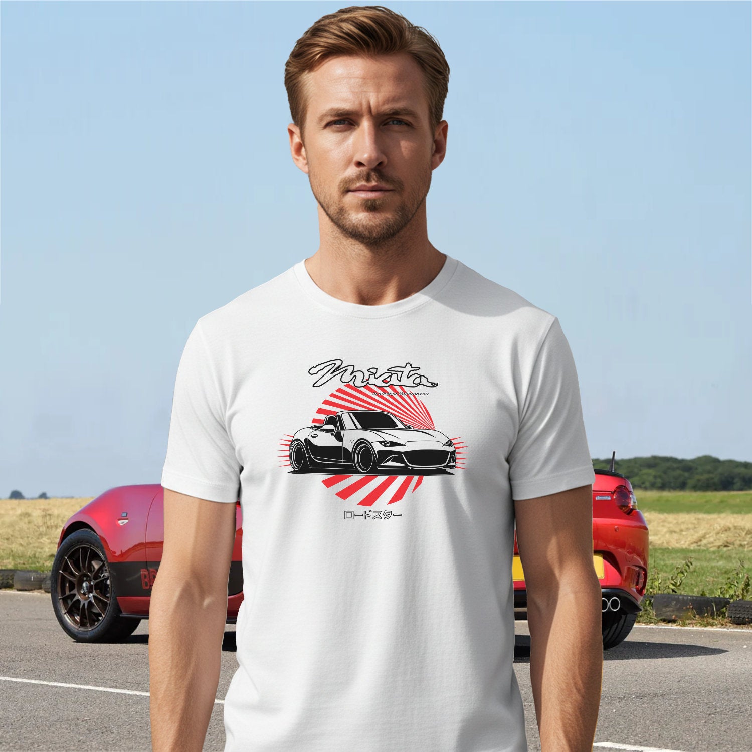 Man wearing a white t-shirt with a car graphic and text, standing on a road with a red car in the background.